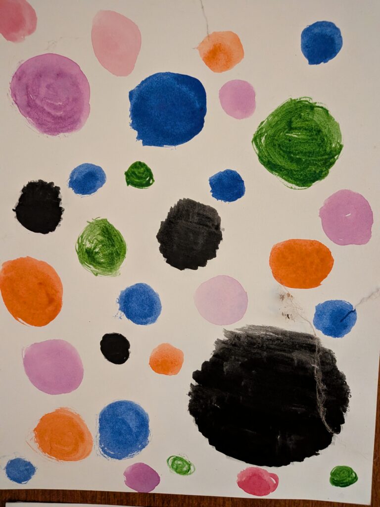 Watercolor: dots of every size and colour scattered across white paper, some black.